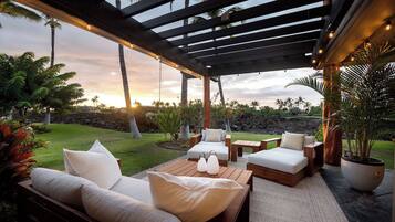An outdoor patio with wooden furniture, a pergola, and a view of the sunset.