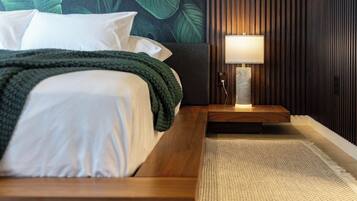 A neatly made bed with white linens and a green throw blanket, a bedside lamp, and a textured rug on a wooden floor.