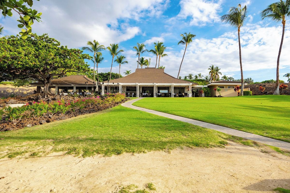 Un resort con un espacio al aire libre cubierto, césped y palmeras.