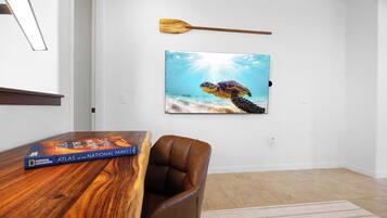 A room with a wooden table, a brown leather chair, a framed picture of a sea turtle, and a book titled 'Atlas of the National Parks'.