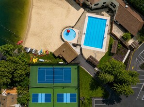 An aerial view of a property with a swimming pool, tennis courts, and a beach area. - Whispering Oaks Walk to Beach & Pool, in Hideout (Hamlin)