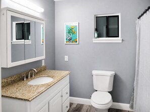 A bathroom with a white sink, a toilet, a framed picture on the wall, and a window above the toilet. - Peaceful 3BR Corner Home w/ Large Yard & Patio Kid and Pet Friendly (Sacramento)
