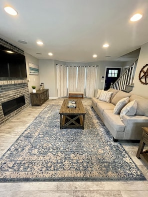 A living room with a fireplace, a sofa, a coffee table, and a patterned rug. - Cozy Lake House 1 - Lakefront Retreat with Private Dock & Fire Pit (Macon)