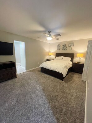 Ein Schlafzimmer mit einem Bett, zwei Nachttischen mit Lampen, einem Deckenventilator und einem an der Wand montierten Fernseher.