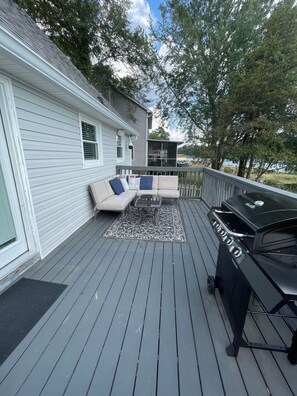 A deck with a grill, outdoor furniture, and a view of a house. - Cozy Lake House 1 - Lakefront Retreat with Private Dock & Fire Pit (Macon)