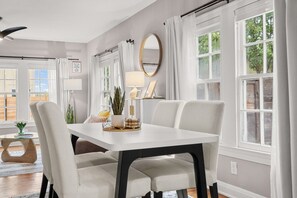 A dining area with a white table, four chairs, a ceiling fan, and a view of the outdoors through large windows. - South Congress Cottage Butcher Block Kitchen String-Lit Lounge + Outdoor TV (Austin)