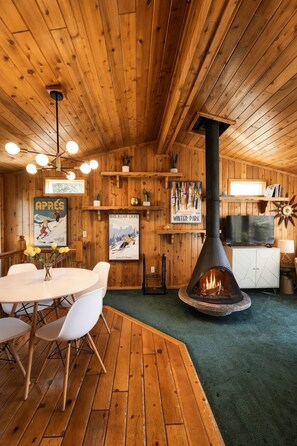 A wooden interior with a fireplace, a dining area, and a television. - Sierra Chalet - Celebrity Vacation Homes (Big Bear Lake)