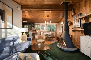 A cozy cabin interior with a sofa, chairs, a dining table, a fireplace, and a kitchen area. - Sierra Chalet - Celebrity Vacation Homes (Big Bear Lake)