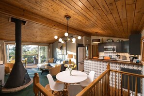A cozy cabin interior with a dining area, kitchen, and a large fireplace. - Sierra Chalet - Celebrity Vacation Homes (Big Bear Lake)