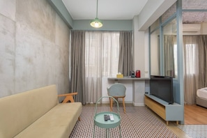 Una sala moderna con un sofá, una mesita, una silla, un televisor y un escritorio con una computadora.