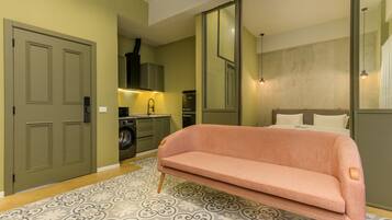 Habitación de hotel compacta con sofá, lavadora, cama y un espejo grande.