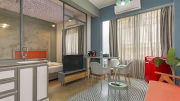 Une chambre d’hôtel compacte comprenant un coin cuisine, un lit, une télévision, un coin repas avec des chaises et une grande fenêtre avec des rideaux.