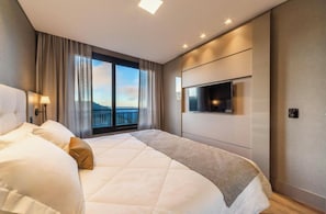 A modern hotel room with a large bed, a TV mounted on the wall, and a view of the outdoors. - Vrbo Property (Gramado)