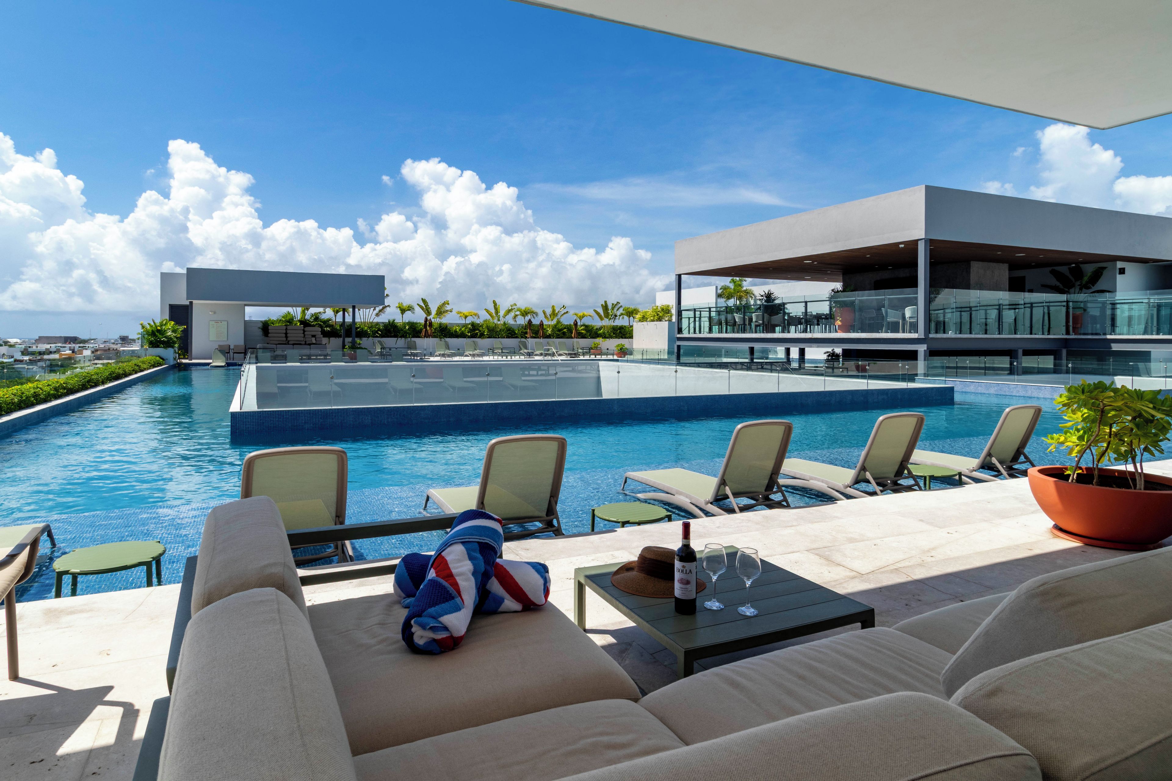 A rooftop pool area with lounge chairs, a sofa, and a table with a bottle and glasses.