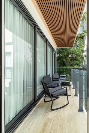 A modern balcony with large glass doors, a wooden ceiling, and outdoor furniture. - Brand-New 2BR at Ceiba25 - Rooftop Infinity Pool, Near Beach & 5th Ave (Playa del Carmen)