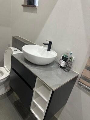 A bathroom with a white sink, black faucet, and a toilet. There are two bottles on the sink counter. - Comrades villa guest house  (Pietermaritzburg)