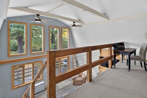 A spacious room with a high ceiling, large windows with wooden frames, a staircase with a wooden railing, a dining table with chairs, and a ceiling fan. - Private Mountainside Retreat | Near Wineries & Bristol Mountain (Naples)