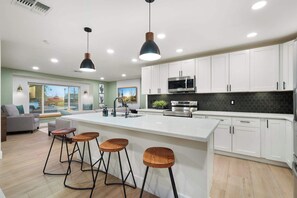 Une cuisine moderne avec des meubles blancs, un îlot central doté de tabourets, un four à micro-ondes et une grande fenêtre.