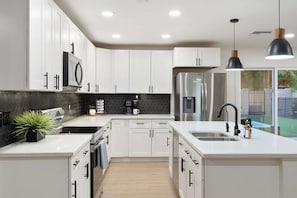 A modern kitchen with white cabinetry, stainless steel appliances, and a central island with a sink. - NEW| Casa Alegre "Happy House"| FREE Heated Pool (Scottsdale)