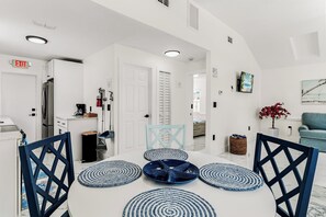 A modern interior with a dining area featuring a white table, blue and white patterned mats, and black chairs. - Turquoise Mermaid Cottage at White Sands | updated 1 br/1ba steps to beach (Indian Rocks Beach)