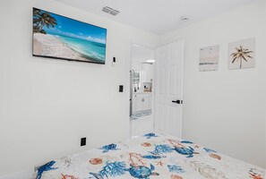 Ein Schlafzimmer mit einem Bett, einem an der Wand montierten Fernseher, einer Tür zu einem Badezimmer und einem kleinen Fenster.