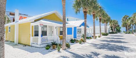 A row of beachside mobile homes with white and blue exteriors, palm trees, and a clear sky.
