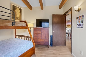 Ein Schlafzimmer mit Etagenbett, einer Holzkommode, einem Fernseher und einer Tür zu einer Küchenzeile.