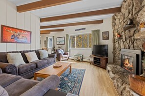 A cozy living room with a stone fireplace, a leather sofa, a television, and a dining area. - Lake Dillon and Mountain Views! (Dillon)