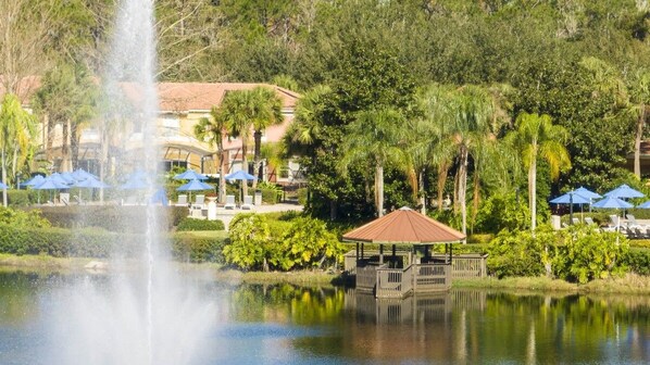 A tranquil outdoor setting with a water fountain, a gazebo, and a poolside area with umbrellas. - Near Disney at Encantada Resort Cozy Townhouse (Kissimmee)