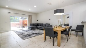 Un saló modern amb un sofà seccional, una taula de dinar de fusta amb quatre cadirees i un finestral gran amb vistes.