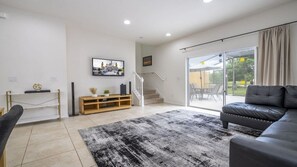 Una sala de estar moderna con un sofá de cuero negro, un mueble de entretenimiento de madera, una escalera y un vidrio que da a un área exterior.