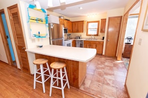 A kitchen with wooden cabinets, a stainless steel refrigerator, a dishwasher, and a sink. There are two bar stools and a window providing natural light. - Oceanside- Near Ocean, Priv Pool, Close to Shopping-SH110 (Duck)