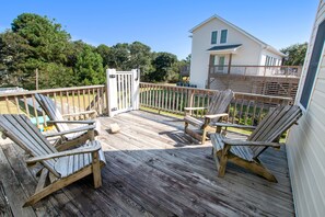 A wooden deck with Adirondack chairs and a small table, surrounded by a wooden fence and a white building in the background. - Oceanside- Near Ocean, Priv Pool, Close to Shopping-SH110 (Duck)