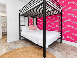 A bunk bed with a white mattress and a single pink pillow, a woven rug on the floor, and a wall with a leopard print wallpaper. - Gorgeous Mountain Sunset Casita with AC Heated Pool Hot Tub Fire pit EV Charger (Palm Springs)
