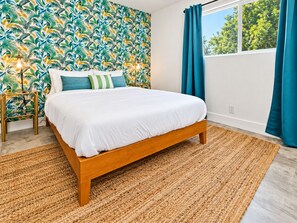 Ein Schlafzimmer mit einem Bett, einer Wand mit Muster, einem Fenster mit Vorhängen und einem Nachttisch mit Lampe.