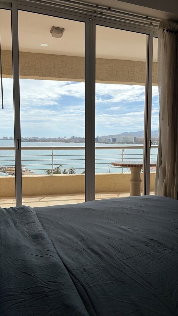 A bedroom with a large bed, a view of the sea, and a balcony with a table.