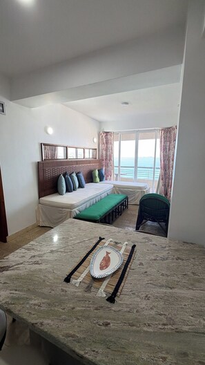 A bedroom with a bed, a bench, a view of the sea, and a dining area with a table.