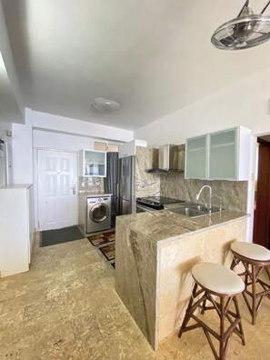 A compact kitchen with a built-in washing machine, a sink, and a marble island with stools.