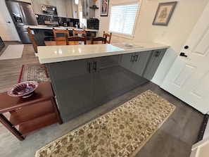 A modern kitchen with a central island, dark grey cabinets, and a dining area with wooden chairs. - Kirkland - Rose Hill Duplex Top Floor Luxurious Oasis + EV (Kirkland)