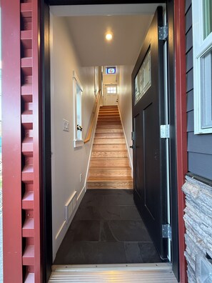 Un pasillo con una escalera de madera que lleva a una puerta con ventana.