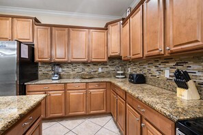 A kitchen with wooden cabinets, granite countertops, a stainless steel refrigerator, and a toaster. - Charming 6 Bedroom House in Kissimmee, 6686 (Orlando)