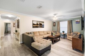 A living room with a sectional sofa, a coffee table, and a television. - Charming 6 Bedroom House in Kissimmee, 6686 (Orlando)