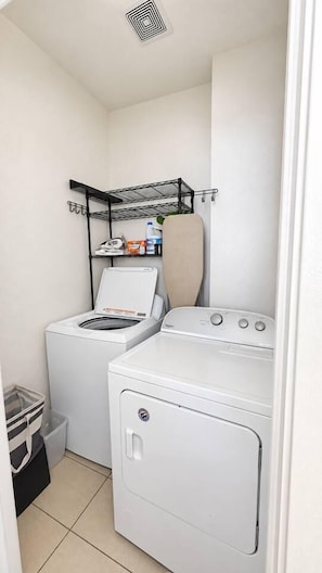 A laundry room with a washing machine, dryer, and shelves with cleaning supplies. - Family Friendly Home w/ Parking & Full Kitchen (Long Beach)