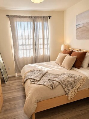 Une chambre à coucher avec un lit, des rideaux, une lampe et un tableau au mur.