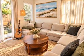 A living room with a sofa, a coffee table, a guitar, and a painting of a beach scene. - Family Friendly Home w/ Parking & Full Kitchen (Long Beach)