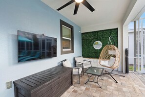 A modern outdoor seating area with a flat-screen TV, a hanging chair, and a wall-mounted sign. - Beautiful Family Home in Davenport City, 6689 (Orlando)