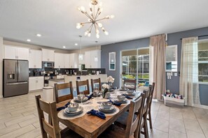 A modern kitchen with white cabinets, a stainless steel refrigerator, and a dining area with a wooden table set for six. - Beautiful Family Home in Davenport City, 6689 (Orlando)