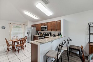 A modern kitchen with wooden cabinets, stainless steel appliances, and a granite countertop. - Cozy Home in Davenport for Your Family, 6700 (Orlando)