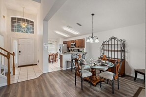 A dining area with a glass-top table, metal chairs, and a chandelier. - Cozy Home in Davenport for Your Family, 6700 (Orlando)