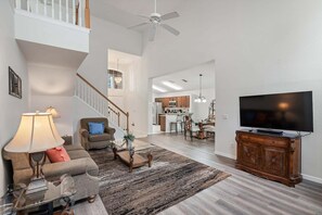 A spacious living room with a high ceiling, a staircase, a dining area, and a kitchen. - Cozy Home in Davenport for Your Family, 6700 (Orlando)